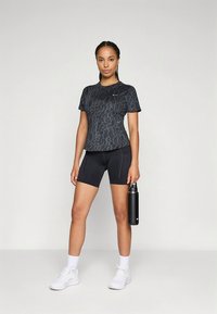 Čierne športové tričko s textúrovaným leopardím vzorom, v kombinácii s čiernymi cyklistickými šortkami a fľašou na vodu. Nosené s bielymi teniskami.