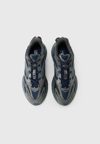 Ett par mörkblå och grå atletiska sneakers med snören, sedd ovanifrån mot en enfärgad vit bakgrund.