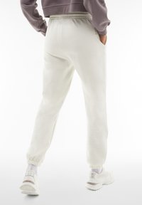Pantalon de survêtement clair avec une taille élastique et des poignets élastiques, comportant des poches latérales et un tissu doux et texturé.