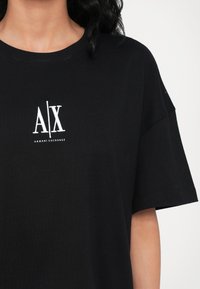Juodas medvilnės marškinėlis su laisvu siluetu. Centre yra baltas "A|X" logotipas ir "ARMANI | EXCHANGE" tekstas. Trumpi rankovės, apvalus iškirpimas.