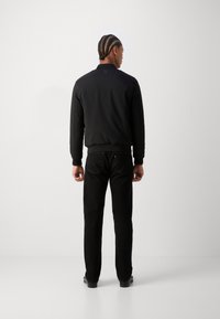 Svart ribbete bomberjakke med krage, iført sorte jeans. Merknad detaljer inkluderer et logo-patch og teksturert stoff.