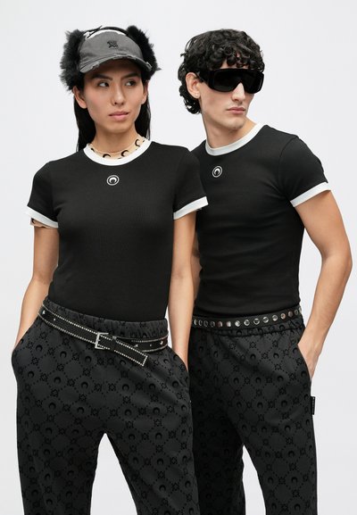 Μαύρα ριμπ κοντομάνικα τοπ με λευκή διακόσμηση, μαύρο παντελόνι με σχέδια, μαύρη ζώνη με καρφιά, γκρι καπέλο με γούνινες λεπτομέρειες, σκούρα γυαλιά ηλίου.