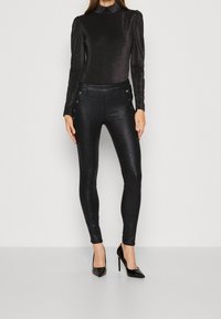 Svarta, glänsande, slim-fit byxor med en slät textur och knappar på sidan. I kombination med en långärmad, glittrande svart topp och höga klackar.