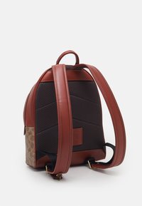 Brązowy plecak skórzany z teksturowanym, czarnym siatkowym tyłem. Posiada złote akcesoria, regulowane paski i boczny wzór z logo.