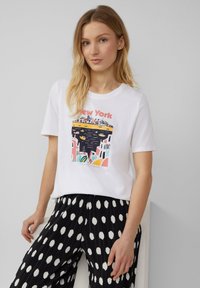 T-shirt blanc à manches courtes avec un graphique coloré de New York. Associé à un pantalon plissé noir orné de grands pois blancs.