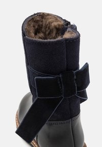 Námořnické modré kotníkové boty s svrškem z semiše, měkkou hnědou podšívkou a sametovou mašlí jako akcentem. Má kulatou špičku a prošívané detaily.