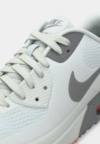 Κοντινή λήψη ενός λευκού και γκρι αθλητικού παπουτσιού Nike Air Max που δείχνει τα κορδόνια, το δίχτυ, τις υφασμάτινες επενδύσεις με υφή και το λογότυπο Swoosh στο πλευρό.