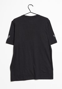 Svart bomullströja hängande på en krok, med korta ärmar, rundad halsringning och en enfärgad baksida med en liten logotyp på vänster ärm.