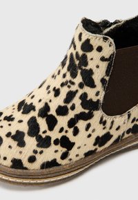 Botín tobillo con estampado de leopardo, fabricado en piel de vaca texturizada en tonos beige y negro, con paneles laterales elásticos y una suela plana marrón.