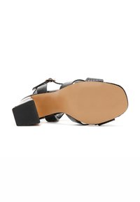 Sandalia negra de tacón con un upper texturizado y tacón rectangular. Presenta correas ajustables y una suela suave de color claro.