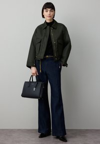 Olivengrønn cropped jakke med store lommer, svart høyhalset genser, vide mørke denimjeans, svart håndveske og spisse svarte sko.