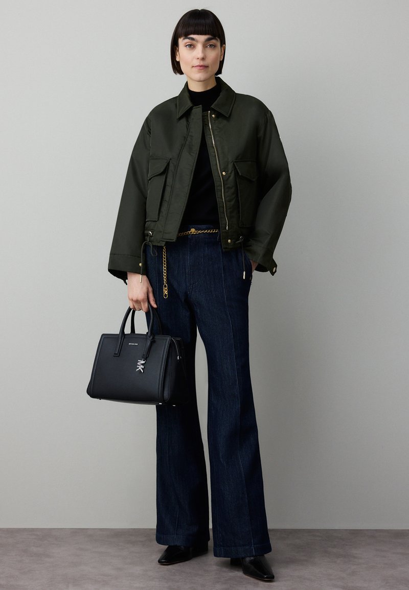 Olivengrønn cropped jakke med store lommer, svart høyhalset genser, vide mørke denimjeans, svart håndveske og spisse svarte sko.