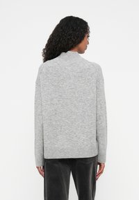 Maglione grigio a maglia con colletto alto, vestibilità ampia, spalle scese e orlo a costine. Il tessuto appare morbido con una texture liscia.
