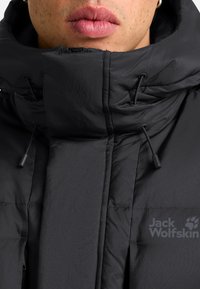 Zwarte pufferjack met een hoge kraag, voorzien van een matte textuur, trekkoord en logo aan de linkerzijde.