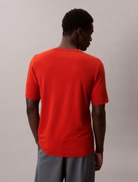 T-shirt de algodão vermelho com mangas curtas e decote redondo, apresentando uma textura suave e um corte descontraído, visto de trás.