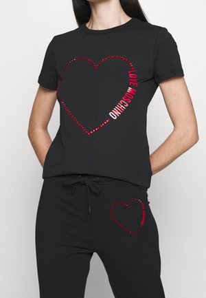 Vrouw draagt een zwarte set met een top met korte mouwen en een broek met rode kralen hartomtrekken en tekst "LOVE MOSCHINO" op beide stukken.