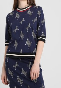 Mörkblå topp med korta ärmar, prydd med ett leopardskinnsmönster och svarta och krämfärgade ränder längs halsringningen och fållen.