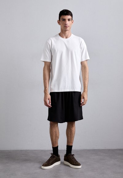 White cotton t-shirt with short sleeves, paired with black athletic shorts. Footwear includes dark brown suede sneakers with cream soles.