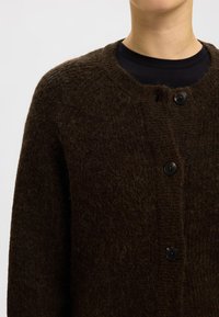 Rjava pletena jopica z okroglim izrezom, sprednjim gumbom in teksturirano tkanino z mehkim, puhastim videzom.