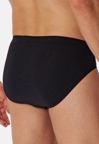 Zwarte katoenen slips met een strakke pasvorm, gladde textuur en elastische tailleband. Het ontwerp is eenvoudig en minimalistisch, zonder zichtbare patronen.
