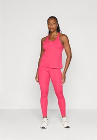 Tett rosa trenings tanktop og tights laget av elastisk stoff. Har et lite hvitt logo på brystet og anklene. Bæres med hvite sneakers.