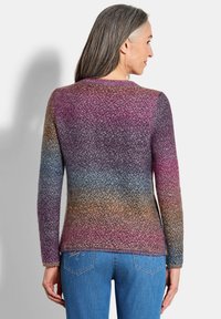 Femme aux cheveux gris portant un pull en tricot à manches longues avec un dégradé de tons violets, bleus et marron, assorti à un jean bleu, vue de dos.