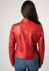 Rode leren jas met een aangesloten ontwerp, voorzien van een ingeknipte kraag en zichtbare naden, gecombineerd met blauwe denim jeans.