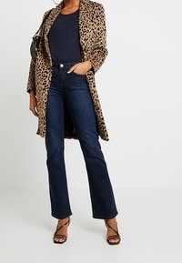 Leopard print coat, navy top, dark flared jeans, and strappy heels. Features a mid-length design and smooth textures. Black handbag included.