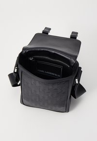 Borsa a tracolla nera con un design geometrico testurizzato, una tasca con cerniera all'interno e spallacci regolabili. Realizzata in pelle liscia.