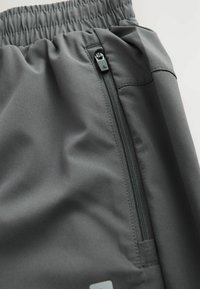 Shorts deportivos grises hechos de un tejido suave con una cinturilla elástica y un bolsillo con cremallera lateral, con costuras limpias y un detalle minimalista.