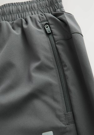 Shorts deportivos grises hechos de un tejido suave con una cinturilla elástica y un bolsillo con cremallera lateral, con costuras limpias y un detalle minimalista.