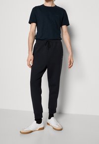 Mörkblå kortärmad t-shirt tillsammans med mörka sweatpants, som har en elastisk midja och uppvikta fållar, kompletterat med vita sneakers.