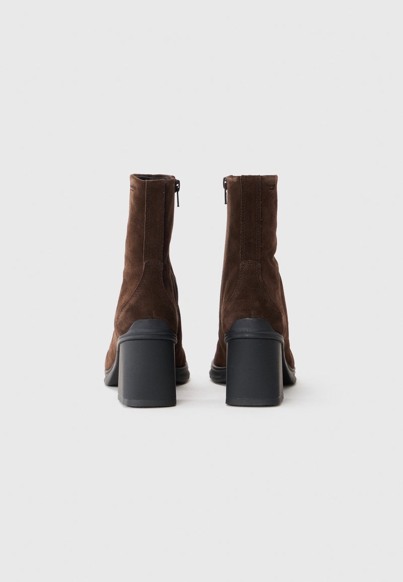 Bottines en suede marron avec un bout rond, un talon bloc noir discernable et un zip sur le côté. La vue arrière met en avant la hauteur et la forme.