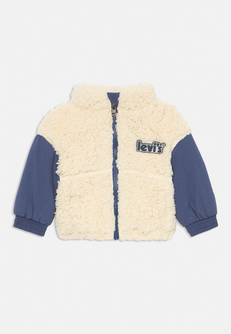 Chaqueta de forro polar con cuerpo crema y mangas azul marino, con cierre de cremallera y acento de logo en el pecho. Textura suave y puños elásticos.
