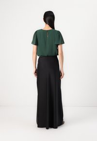 Grüne Chiffonbluse mit kurzen Puffärmeln, kombiniert mit einem bodenlangen schwarzen Satrock, der eine glatte Textur und einen subtilen Glanz aufweist.
