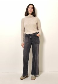 Lichtbeige coltrui, grijze wijde jeans met zakken en grijze sneakers. Zachte textuur en casual pasvorm. Eenvoudig ontwerp.