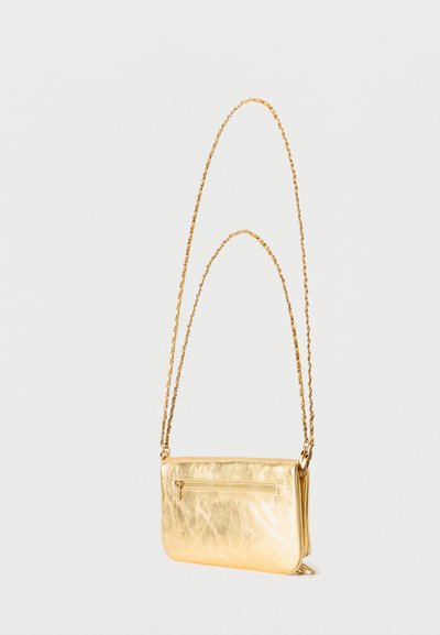 Χρυσή δερμάτινη τσάντα ώμου με μακρύ αλυσίδα ιμάντα και μικρή εξωτερική τσέπη με φερμουάρ στο μπροστινό μέρος, σε λευκό φόντο.