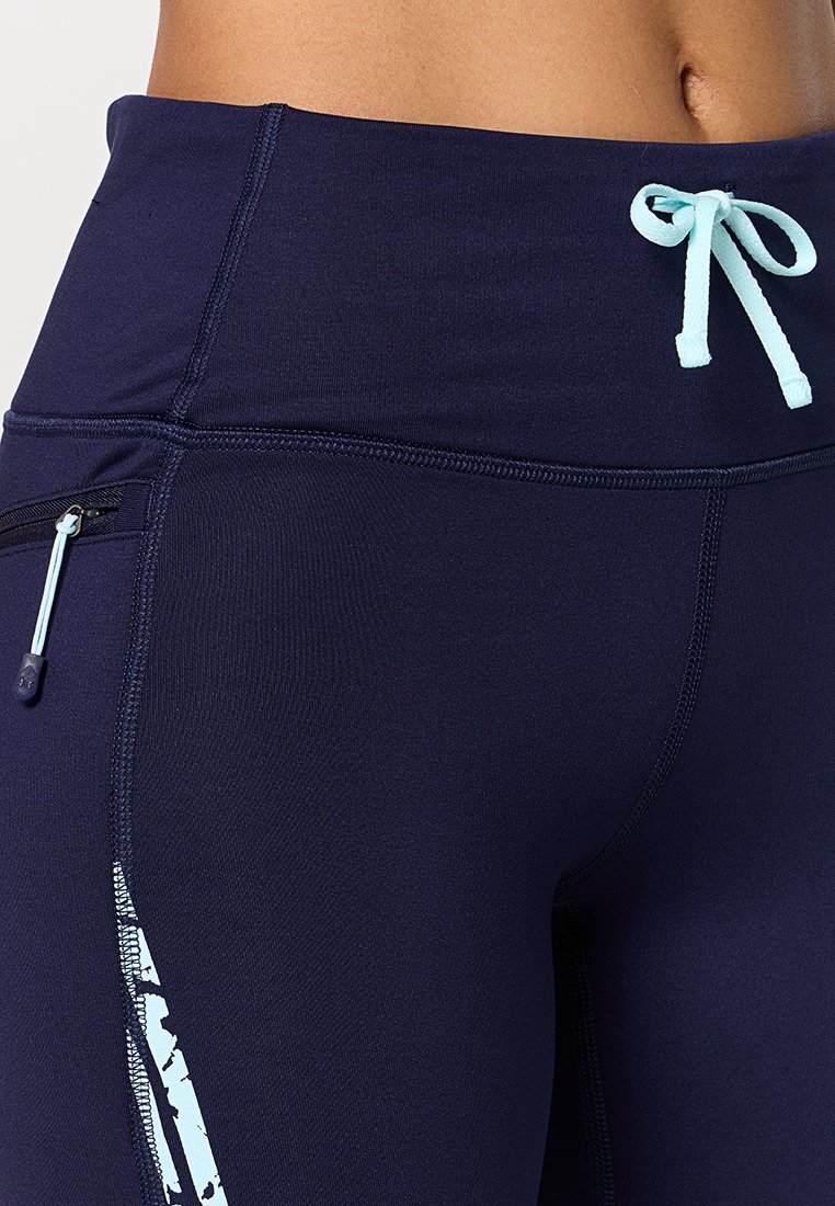 Leggings azul marino con cintura alta, detalle de cordón en azul claro y un bolsillo lateral con cremallera. Tela suave y elástica con acentos impresos.