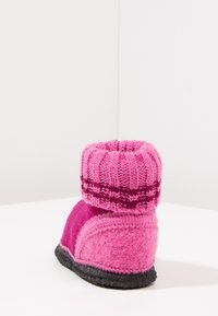 Roze vilten slipper met een gebreide rand. Heeft een effen roze lichaam en een gestructureerde donkere zool. De rand heeft een gestreept patroon in donkerdere roze tinten.