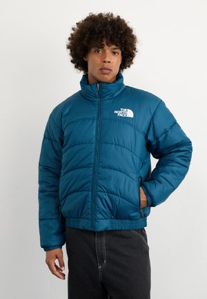 Teal puffer jacket with zip closure, high collar, and white logo detail. Features horizontal quilted pattern and elastic cuffs.