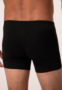 Boxer shorts en coton noir avec une taille élastique, présentant une texture lisse et un ajustement confortable, montrés d'une perspective arrière.