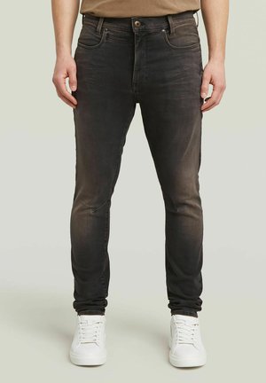 Black denim skinny jeans with a faded wash, five pockets, and a button closure. Worn with white sneakers, featuring a smooth texture.