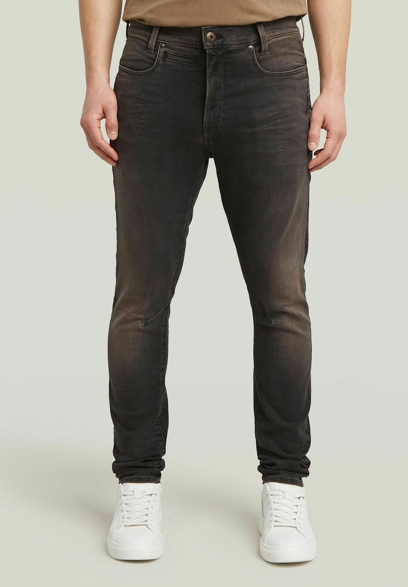 Μαύρο τζιν skinny παντελόνι με φθαρμένο φινίρισμα, πέντε τσέπες και κλείσιμο με κουμπί. Φοριέται με λευκά αθλητικά παπούτσια με λεία υφή.