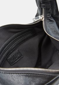 Interno di una borsa nera in pelle con rivestimento in tessuto, dotata di una tasca interna con zip e una cerniera in metallo argento parzialmente aperta.