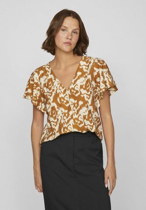Blusa de estampado marrón y crema con escote en V, mangas cortas con volantes y ajuste relajado, combinada con una falda negra. Tejido texturizado.