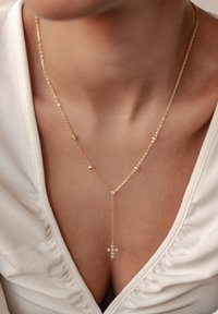 Collar de cadena de oro con un colgante de cruz adornado con pequeñas piedras preciosas claras, que exhibe un diseño delicado y en capas.