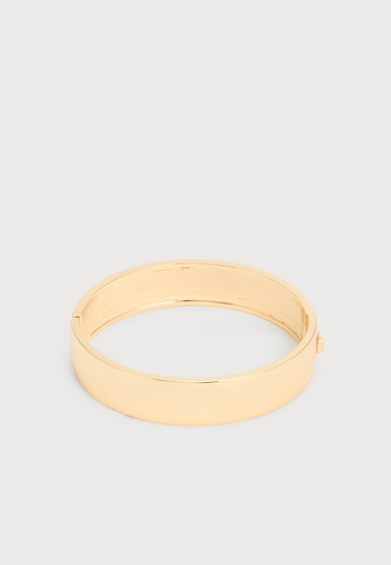 Gyldenfarget metallarmbånd med glatt, polert overflate og en liten lås mot en enkel lys bakgrunn.