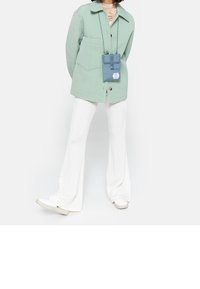 Giacca imbottita verde chiaro con collo, abbinata a pantaloni bianchi a coste svasati e scarpe da ginnastica bianche. È presente una piccola borsa a tracolla blu.