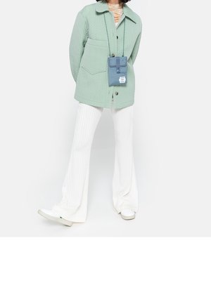 Jasnozielona pikowana kurtka z kołnierzem, zestawiona z białymi prążkowanymi rozszerzanymi spodniami i białymi tenisówkami. Do niej przypięta jest mała niebieska torba na ramię.