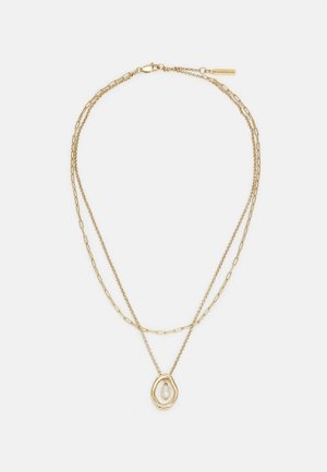 Gouden gelaagde ketting met twee verschillende schakelstijlen en een hanger met een onregelmatig gouden frame waarin een witte parel zit.
